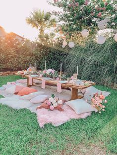 an outdoor picnic setting with pink and white decorations on the grass, candles and pillows