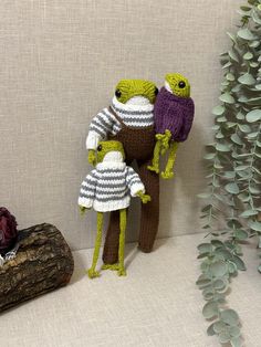 two knitted figures standing next to each other on a white surface with plants in the background