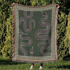 a green and white tapestry with snakes on it in front of some trees, grass and bushes