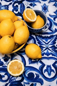 a bowl full of lemons sitting on top of a blue and white table cloth