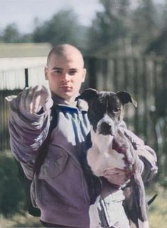 a man holding a dog in his arms and wearing a purple jacket with white stripes