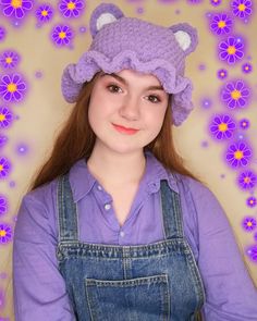 a woman wearing overalls and a purple hat with ears on her head, standing in front of flowers