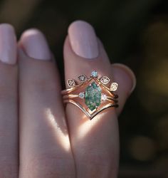 a close up of a person's hand holding a ring with a green stone