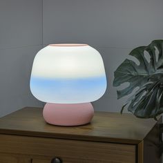 a pink and white lamp sitting on top of a wooden table next to a plant