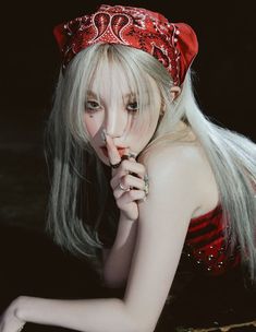 a woman with long white hair wearing a red bandana and holding her finger to her mouth