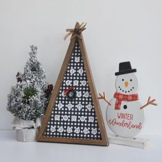 a wooden christmas tree with a snowman decoration next to it on a white surface