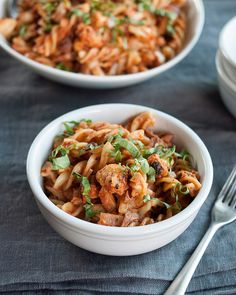 a white bowl filled with pasta and meat on top of a blue cloth next to a fork