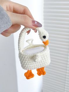 a hand holding a small white crocheted bird ornament with an orange beak