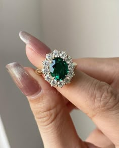 a woman's hand holding an emerald and diamond ring