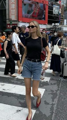 a woman walking across a cross walk in the middle of a busy city with lots of people