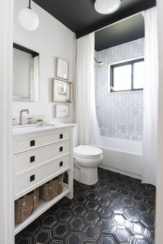 a white toilet sitting next to a bathroom sink under a window with black and white tiles