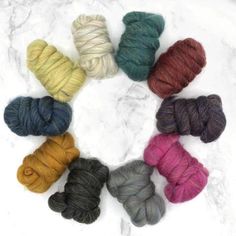 six skeins of yarn arranged in a circle on a marble surface, all different colors