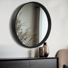 a round mirror sitting on top of a dresser next to a vase filled with flowers