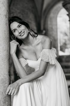 a woman in a white dress leaning against a pillar