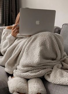 a woman laying on a couch under a blanket using a laptop