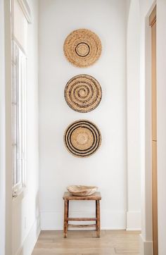 three woven baskets hang on the wall above a wooden bench in a white room with hardwood flooring