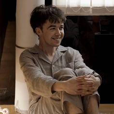 a young man sitting on the floor in front of a window with his arms crossed