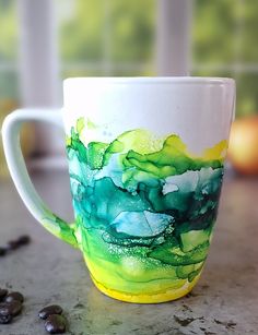 a coffee cup with green and yellow paint on it sitting on a counter next to coffee beans