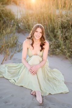 a pregnant woman sitting in the sand at sunset