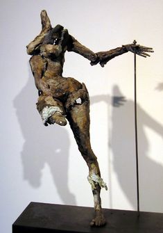 a sculpture of a man holding a stick on top of a wooden block in front of a white wall