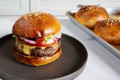 a hamburger on a plate next to some buns and a tray with other rolls