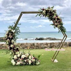 a wedding arch with flowers and greenery on the grass by the beach in front of an ocean