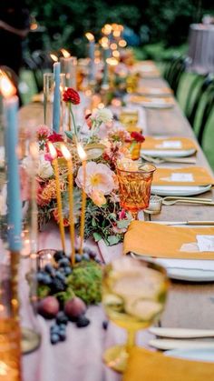 a long table is set with candles and plates for an elegant dinner party in the garden