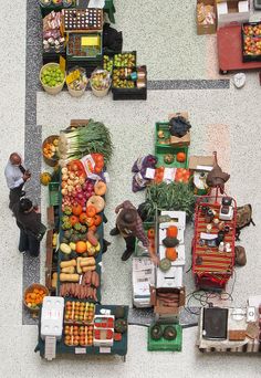 an overhead view of several fruits and vegetables on display at a farmers market with people standing around