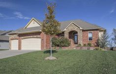 a brick house with two garages and a tree in the front yard on a sunny day