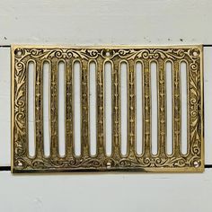 a gold metal grate with decorative designs on the front and sides, set against a white wall