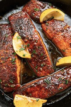 two pieces of fish in a pan with lemon wedges