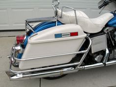 a white and blue motorcycle parked in front of a garage door with its seat up