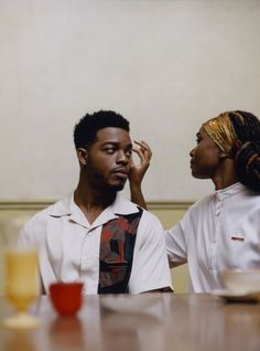 a man and woman sitting at a table with drinks in front of them, looking into each other's eyes