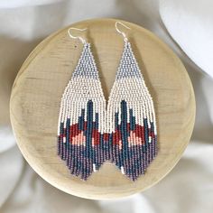 a pair of beaded earrings sitting on top of a piece of wood next to a white cloth