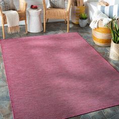 a red rug is on the floor in front of some chairs and potted plants