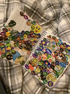 an open notebook with stickers on it sitting on a plaid bed spread in front of the camera