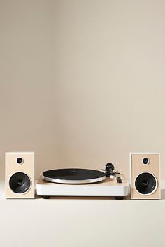 a turntable with speakers on top of it in front of a beige wall and floor