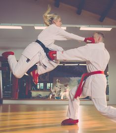 two people in white uniforms are doing karate moves on a wooden floor while one person is wearing red shoes