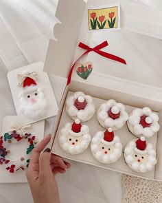 a person is holding a box with some cupcakes in it and santa's hat on top