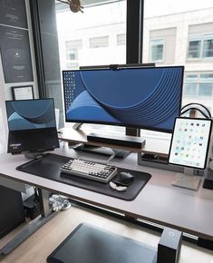 a computer desk with two monitors and a keyboard on it in front of a window