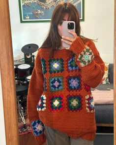 a woman taking a selfie in front of a mirror wearing an orange crocheted sweater