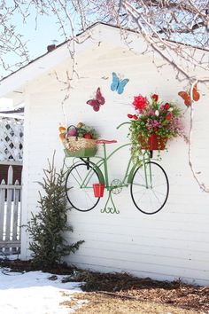 a bicycle with flowers on it hanging from the side of a white building next to a tree