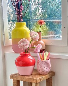 three vases with flowers in them sitting on a small wooden table next to a window