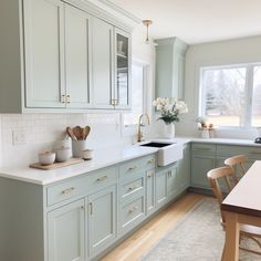 a kitchen filled with lots of green cabinets and white counter tops next to a wooden dining table