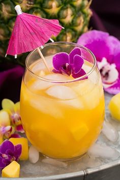 a pineapple drink with purple orchids and an umbrella on the table next to it