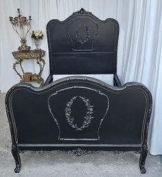 a black bed frame with a wreath on the headboard and foot board in front of a white curtained wall