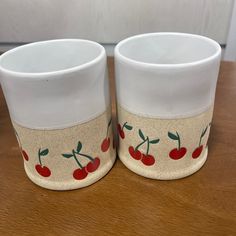 two cups with cherries painted on them sitting on a table