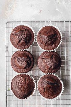 six chocolate muffins cooling on a wire rack, with one cut in half