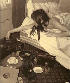 a woman laying in bed next to an old record player and other items on the floor