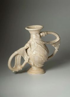 a white vase sitting on top of a table next to a gray wall and floor